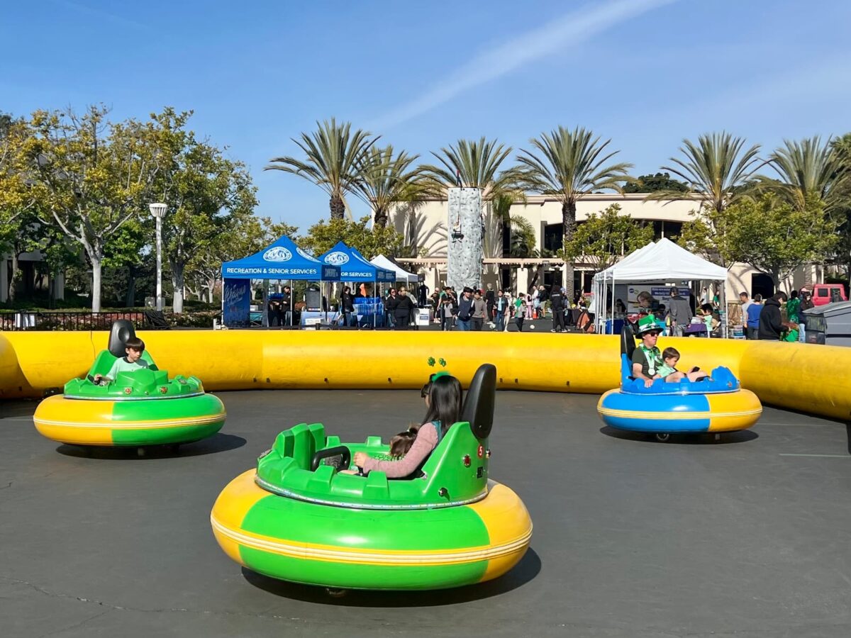 Children riding bumper cars at the Newport Spirit Run Expo with a rock climbing wall in the background